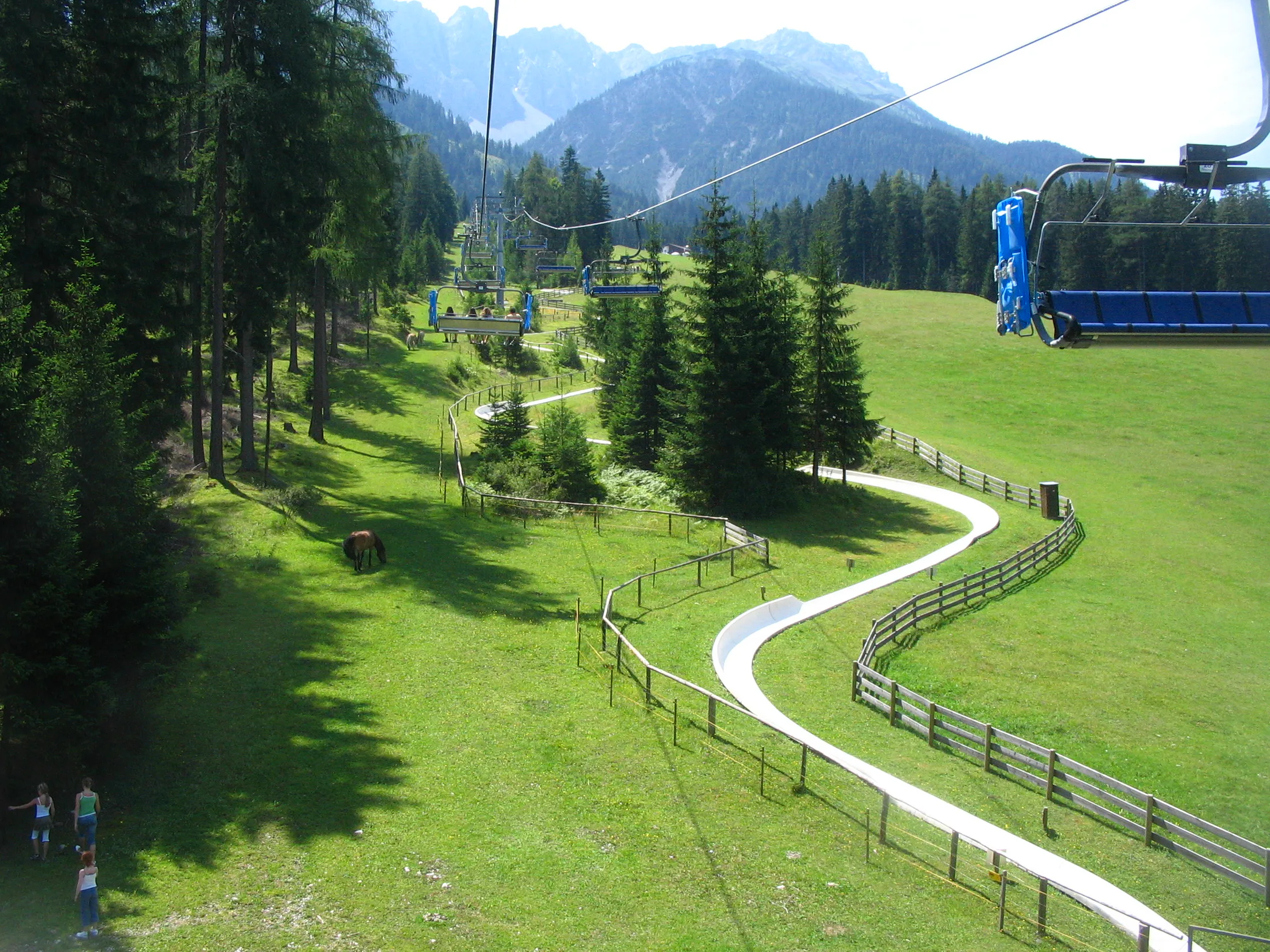 A summer alpine slope with a chairlift, trees, and a long slide.