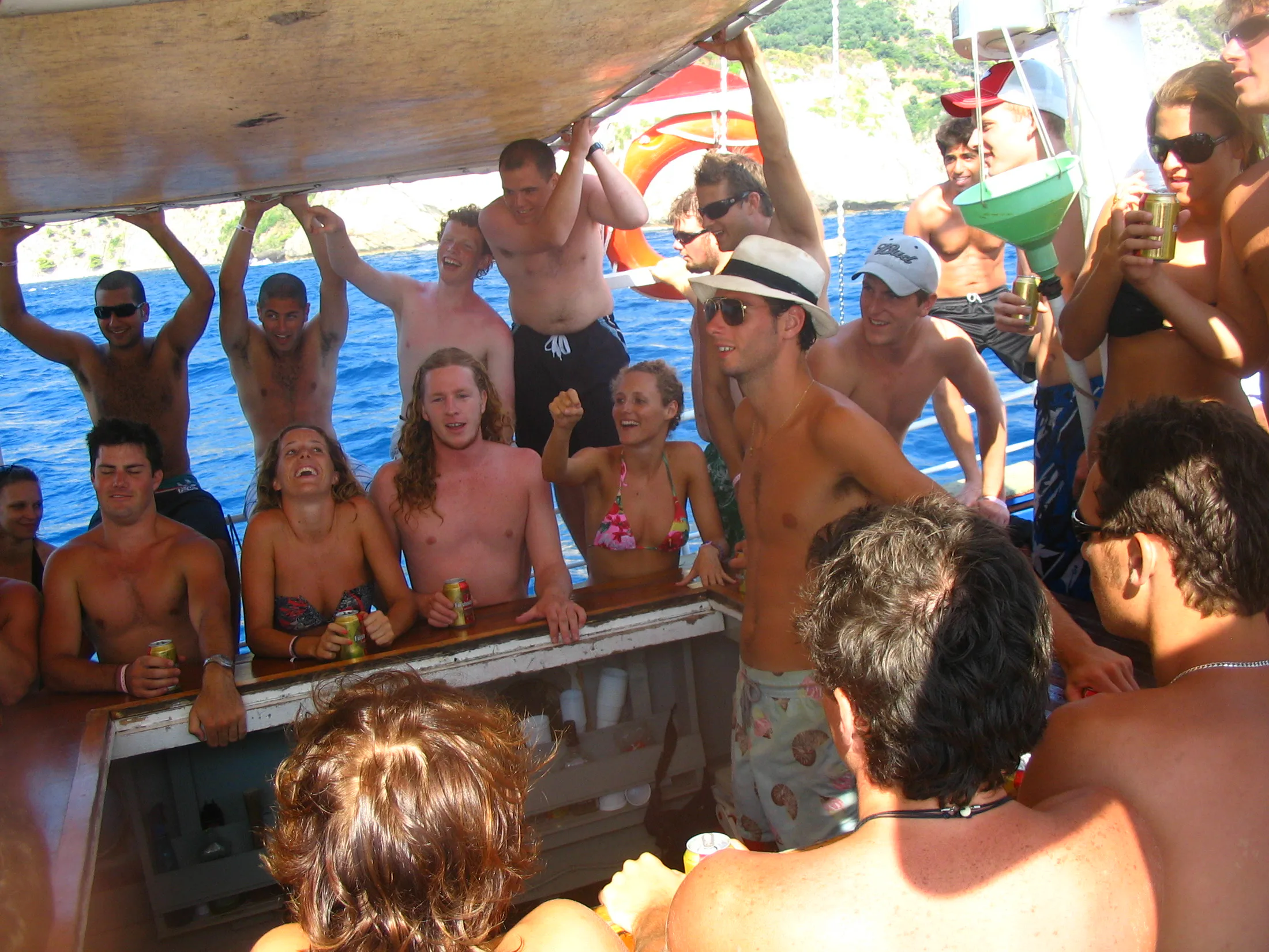 A crowded boat deck with people gathered on bright blue water.