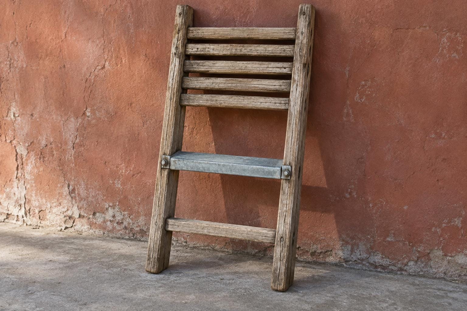 A weathered wooden ladder leans against a russet wall. Five wooden rungs crowd its upper half, while a single galvanized-steel tread bridges a wide gap above the bottom wooden rung.