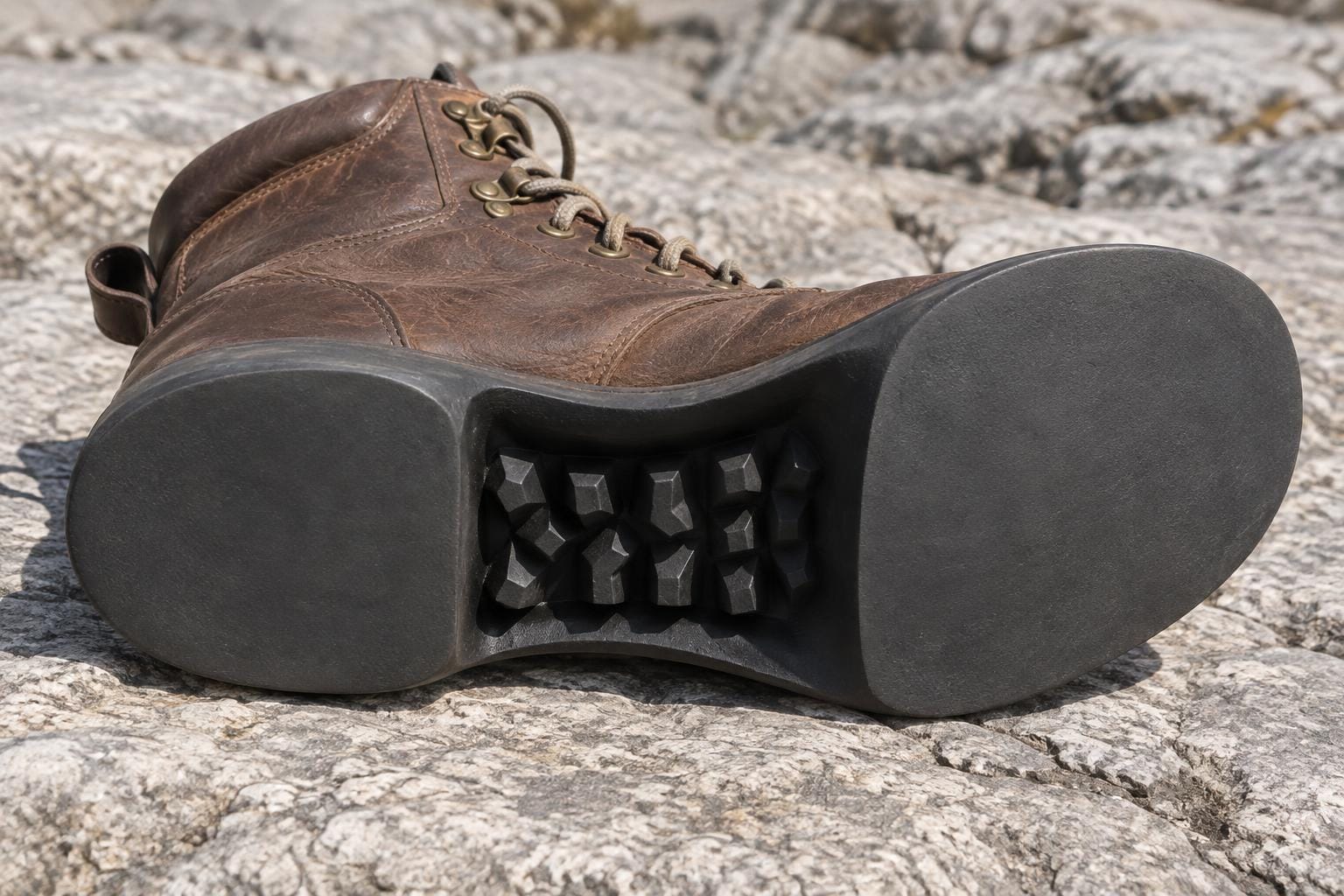 A brown leather boot lies on its side, exposing a sole with smooth heel and forefoot pads and chunky rubber tread tucked entirely inside its deeply recessed arch.