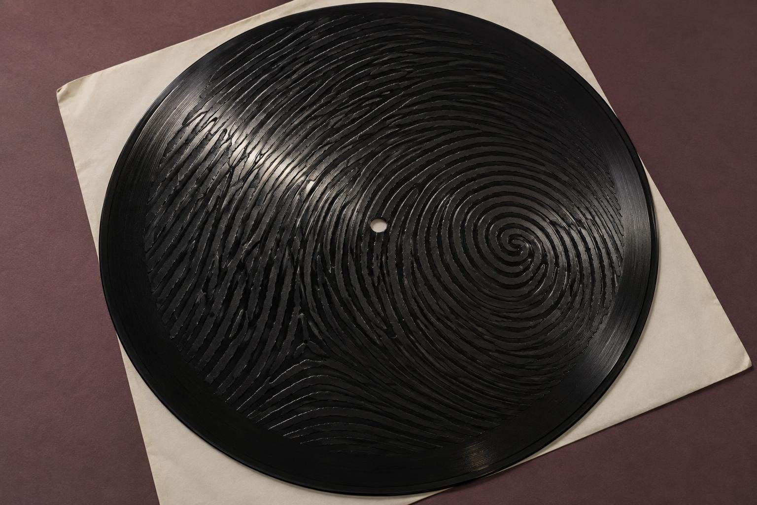 A black vinyl record rests on a blank white sleeve. Its grooves form a giant fingerprint, with branching ridges and a whorl surrounding an offset spindle hole.