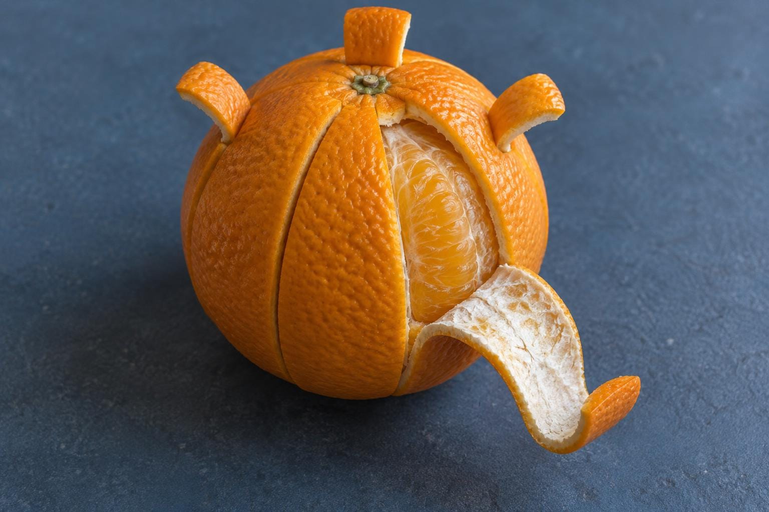 An orange divided into separate rind covers with pull tabs. One cover curls outward to reveal a juicy segment while the others remain closed.