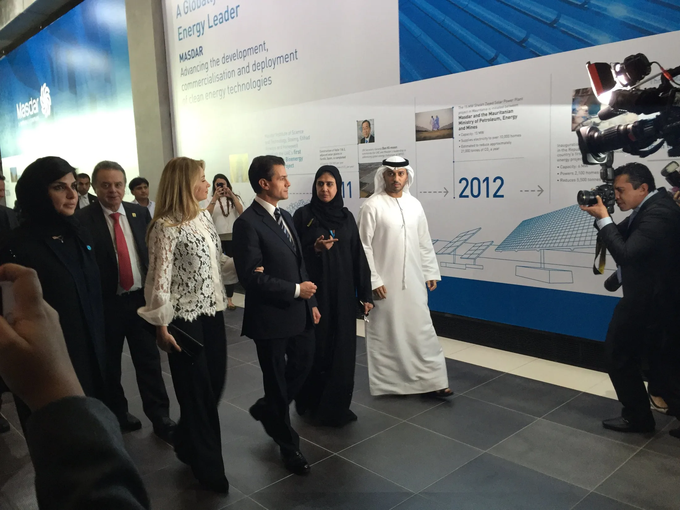 A delegation and press cameras at a Masdar clean-energy exhibit.
